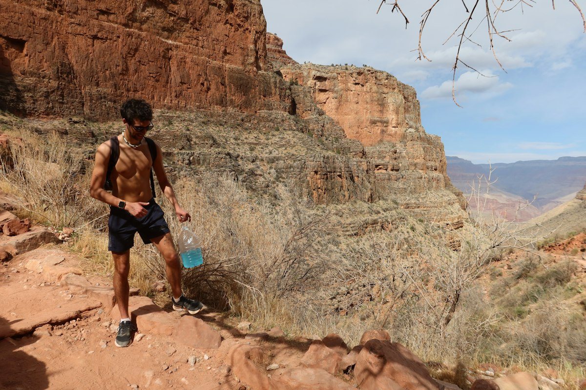 A hiker carrying a water bottle on a red rock canyon trail