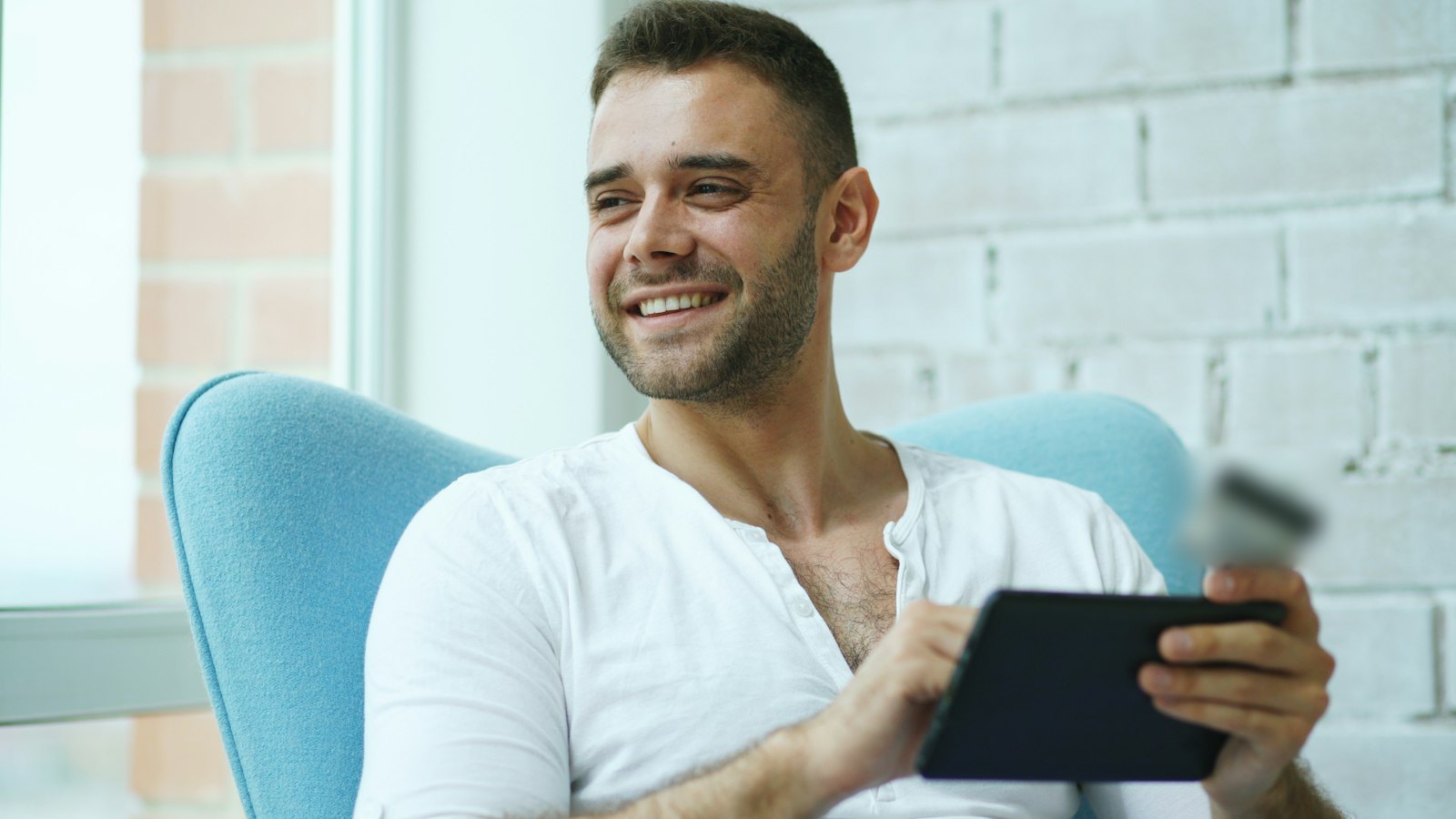 A smiling man shopping online on a tablet in a bright room